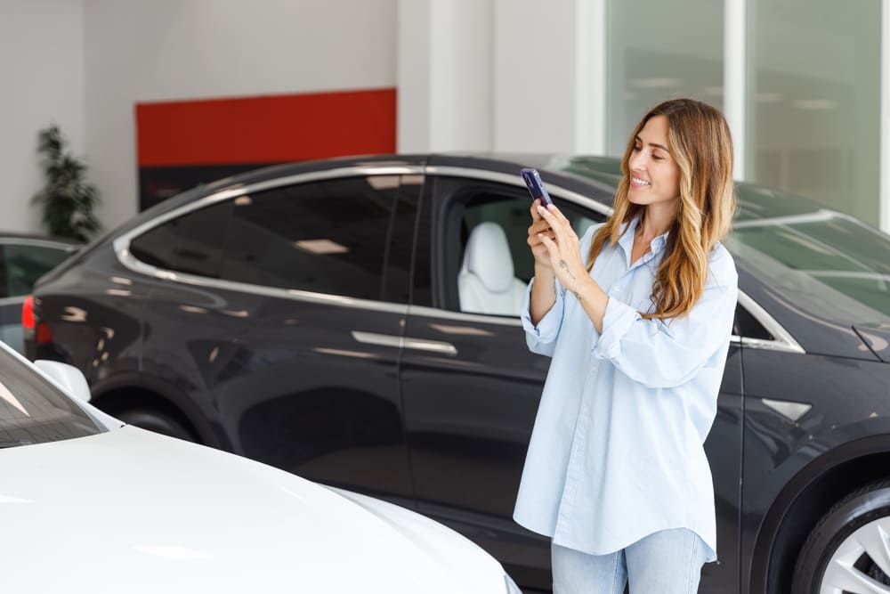 Na imagem vemos uma mulher numa loja de carros tirando foto de um automóvel com seu smartphone. Esta imagem representa a inovação no setor automotivo que deve ser cada vez mais influenciado pelo digital.