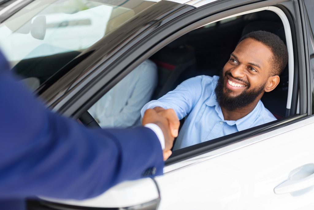 Homem negro sentado dentro do carro novo e apertando a mão do vendedor