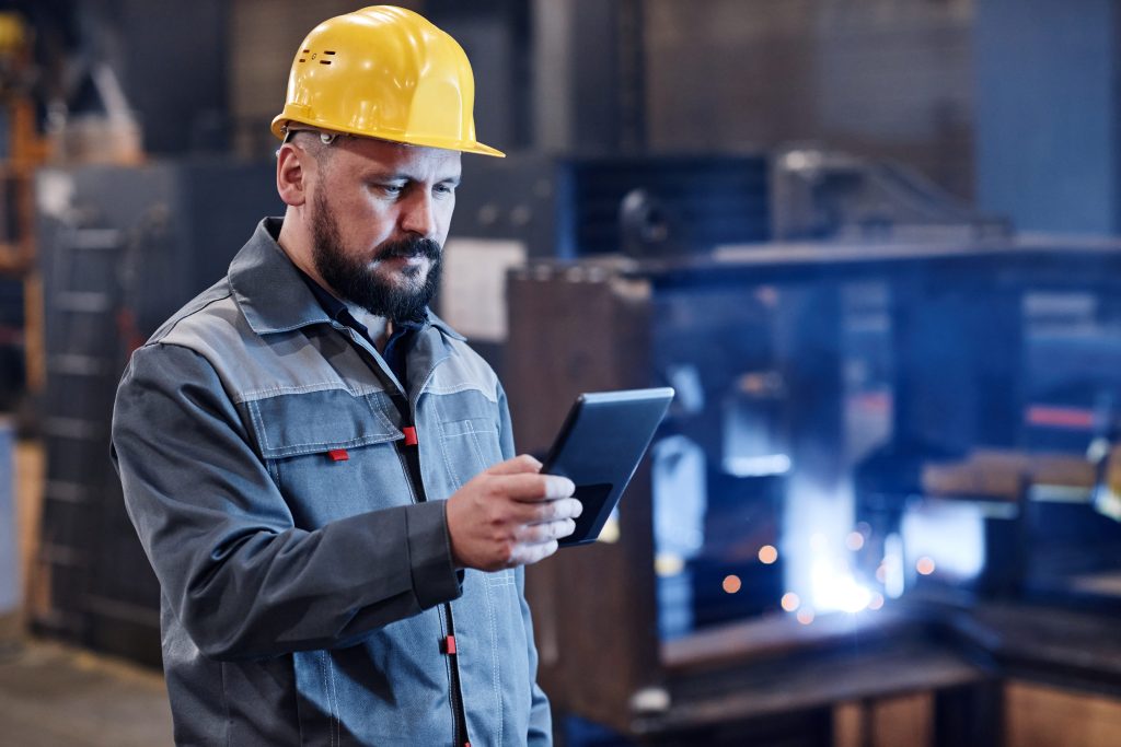 Engenheiro ou construtor masculino em roupas de trabalho usando tablet para verificar dados sobre mercadorias representando a importância dos sistemas para construtoras.