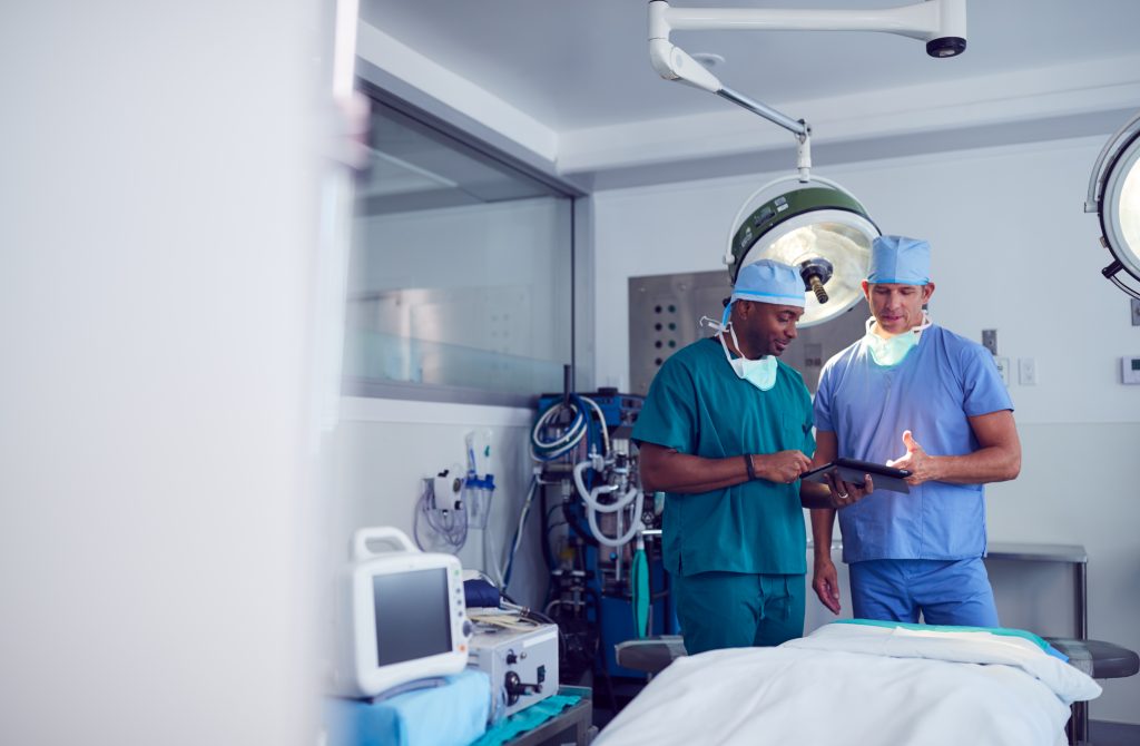 Dois homens cirurgiões vestindo Scrubs olhando para tablet digital no hospital